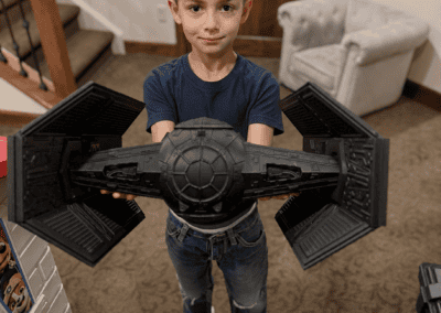 Young boy holding a Star Wars TIE Fighter toy in a cozy home setting.